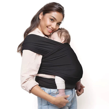 Mother wearing black baby wrap carrier with sleeping newborn secured against chest, white background