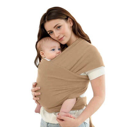 Mother wearing beige baby wrap carrier with alert infant looking outward, showing ergonomic support design