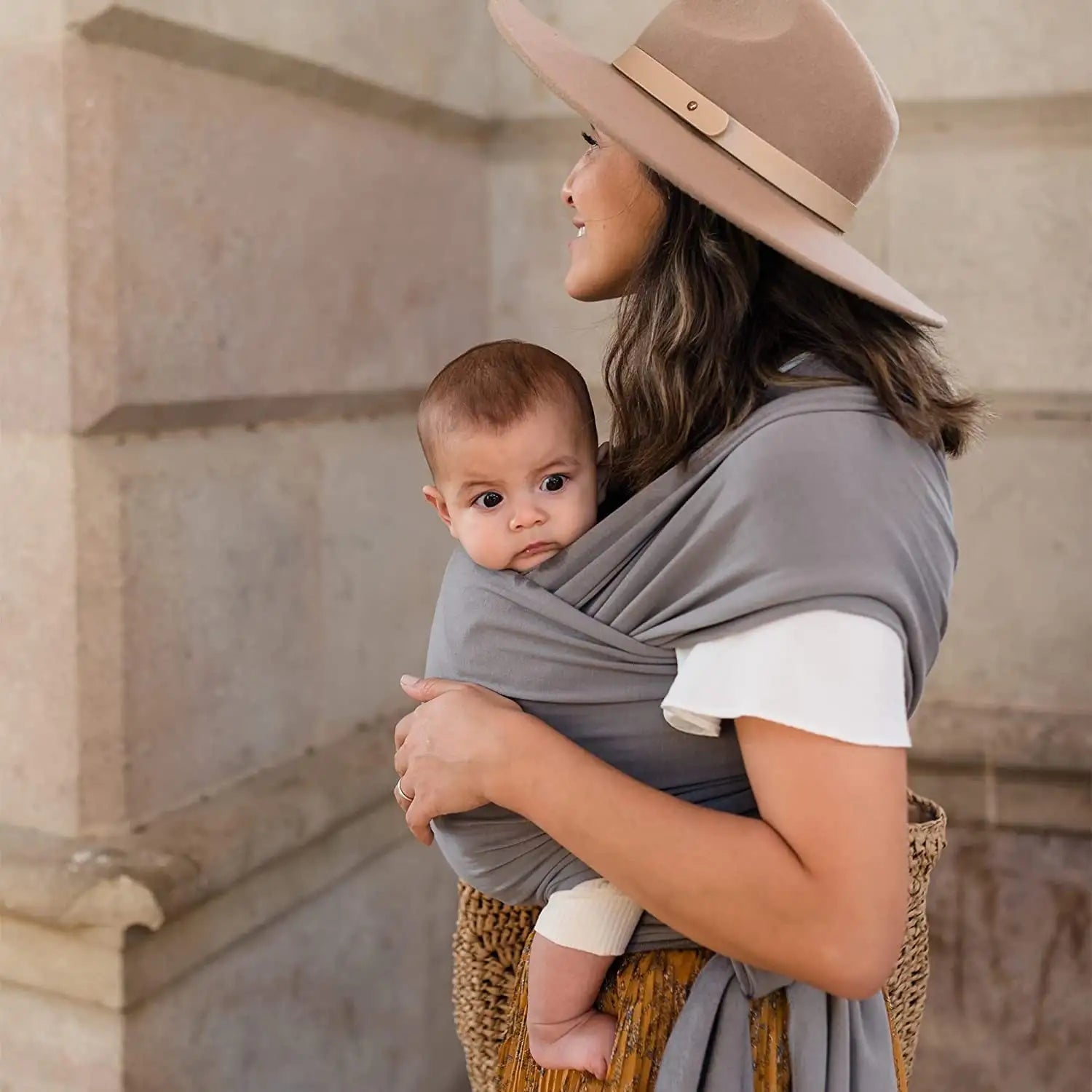 Mother wearing gray baby wrap carrier in home setting, lifestyle shot showing hands-free convenience for daily activities
